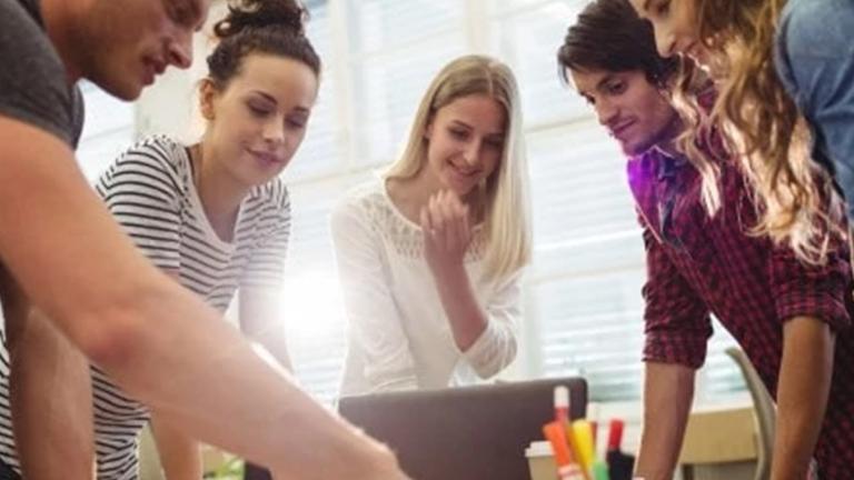 Personas colaborando y mirando sobre una mesa de trabajo.